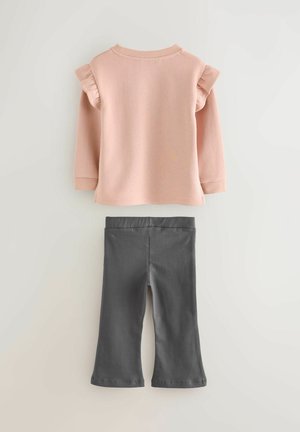 Hellrosa langärmliges Oberteil mit Rüschenschultern, kombiniert mit dunkelgrauen, ausgestellten Hosen, beide aus weichem, elastischem Material.