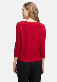 Roter gerippter Pullover mit runder Ausschnitt und Dreiviertelärmeln. Das Material wirkt weich, strukturiert und sitzt tailliert.