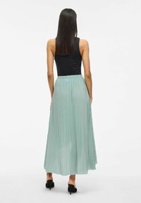Pleated maxi skirt in light mint green with an elastic waistband, paired with a black sleeveless top, features a flowing design and smooth texture.