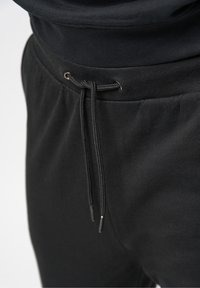 Svarta träningsbyxor med dragsko i midjan, med en slät textur och metalliga detaljer i silverton på dragskons ände.