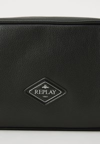 Black textured leather bag with a diamond-shaped logo. The logo features "REPLAY" and "1981" in white on a black background.