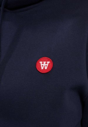 Námořnická modrá mikina s kapucí z texturované látky, na které se nachází kulatý červený znak se bílým logem "W". Jednoduchý design, žádné další viditelné detaily.