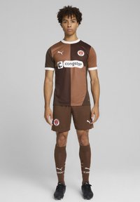 Kit de football marron et beige avec un design en sections. Comprend un logo et un sponsoring sur la poitrine, associé à un short et des chaussettes assortis.