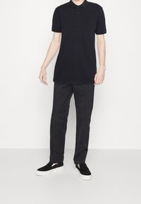 Polo nero a maniche corte, abbinato a pantaloni neri e scarpe slip-on nere. Design casual e minimalista con una vestibilità rilassata.