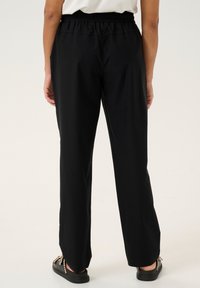 Pantaloni neri con una vestibilità rilassata, vita elastica e gambe dritte. Il tessuto appare liscio con una leggera lucentezza. Indossati con sandali flat.
