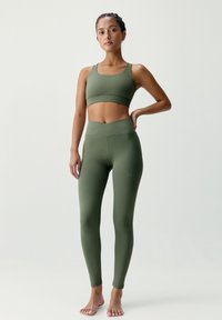 Sada sportovní podprsenky olivově zelené barvy a legín s vysokým pasem. Hladká, pružná tkanina s matným povrchem. Bez viditelných vzorů nebo ozdob.