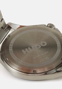 Fondo de acero inoxidable de reloj con logotipo y texto grabados, que presenta una superficie metálica lisa y un detalle resistente al agua, reflejando la luz.
