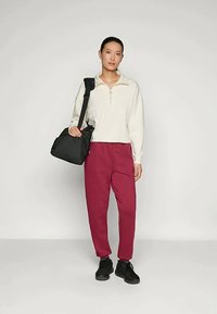 Zwarte schoudertas, crèmekleurige zip-up sweater, bordeauxrode broek en zwarte schoenen. Zachte textuur, casual ontwerp en getailleerde silhoutte.