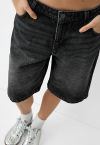 Black denim shorts feature a relaxed fit with a faded texture. The waistband is buttoned and includes side pockets.