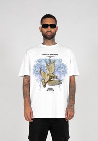 Hvid bomulds t-shirt med et grafisk motiv af to duer mod en blå baggrund, med teksten "VINTAGE DREAMS" ovenfor og "SEASON 2022" nedenfor.