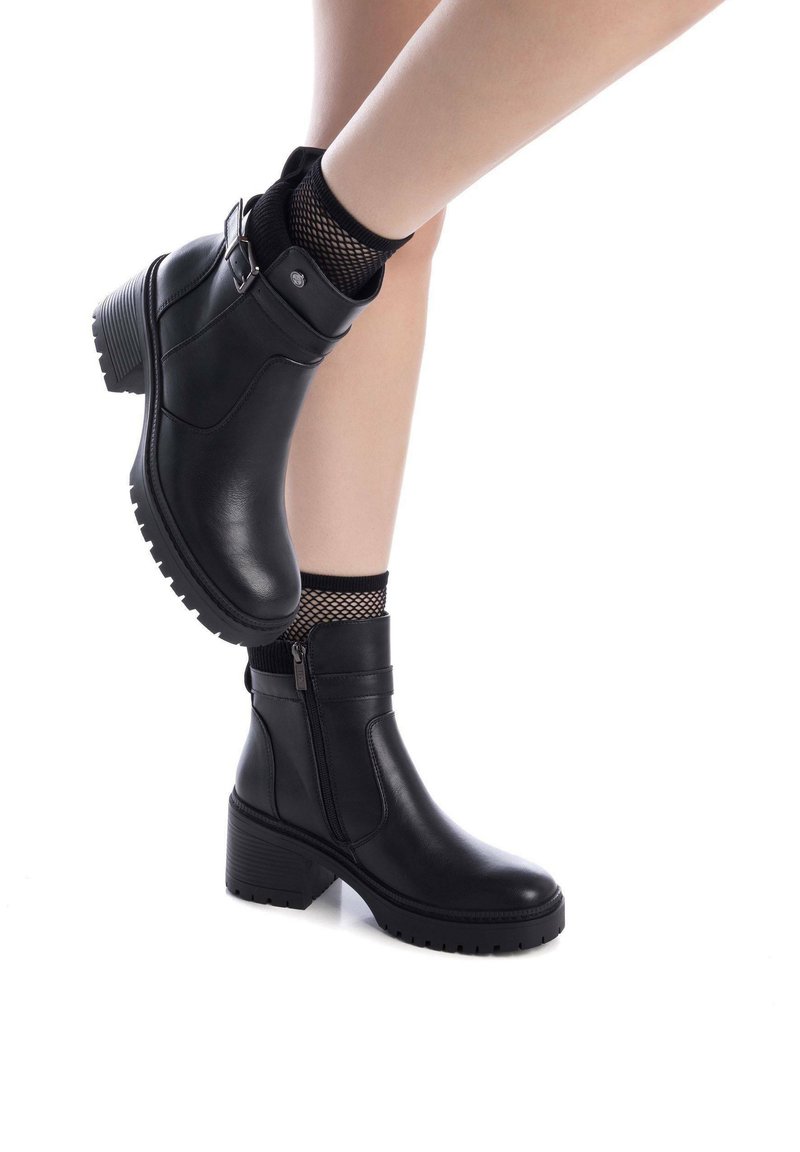 Stivaletti neri in pelle con tacco spesso e chiusura con zip, dotati di una calza nera strutturata con design a rete vicino alla caviglia.