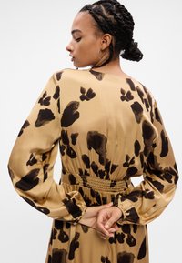 Φόρεμα μακρύ μανίκι σε μπεζ σατέν με καφέ λεοπάρ μοτίβο. Διαθέτει ελαστική μέση και π gathered μανίκια για άνετη εφαρμογή.