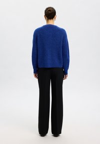 Niebieski, teksturowany sweter z długimi rękawami i ściągaczami na mankietach. W połączeniu z wysokim stanem czarnych spodni. Prosta, luźna sylwetka.