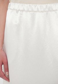 White satin skirt with a gathered elastic waistband, featuring a smooth texture and subtle sheen. Hand resting against the fabric.