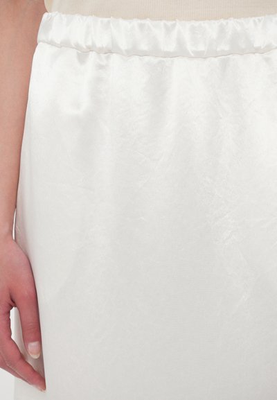 Hvit sateng skjørt med en samlet elastisk midje, kjennetegnet ved en glatt tekstur og subtil glans. Hånd som hviler mot stoffet.