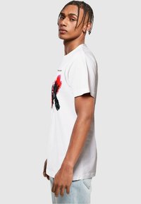 White cotton t-shirt featuring red and black graphic design on the front. Short sleeves, crew neck, standard fit. Light texture.