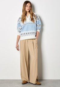 Jasnoniebieski sweter dzianinowy z geometrycznymi wzorami i białym kołnierzykiem, w połączeniu z beżowymi spodniami w szerokie nogawki i brązowymi butami na slip-on.