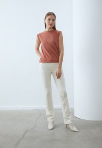 Top de algodón color óxido con acentos de encaje en los hombros, combinado con pantalones ajustados blancos y tacones de malla blancos de punta afilada. Diseño minimalista.