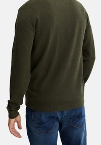 Tmavě zelený svetr s texturou, s žebrovaným lemem a manžetami, kombinovaný s modrými džínami s obloukovými zadními kapsami.