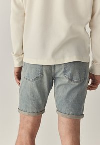 Lichtblauwe denim shorts met opgerolde zomen, vijfzakkenontwerp en subtiele vervaging. Gecombineerd met een crèmekleurige geribde longsleeve.