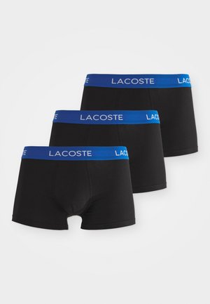 Trois boxeurs noirs avec une ceinture bleue arborant le logo "LACOSTE" en blanc. Fabriqués en matière extensible, conçus pour le confort.