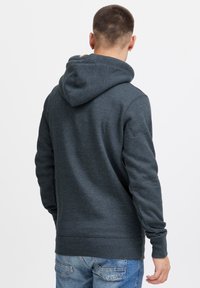 Hoodie gris charbon avec une texture douce, doté d'une capuche avec cordon de serrage et de poignets côtelés, associé à un jean bleu clair.