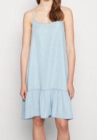 Světle modré, bezrukávové šaty z denimové tkaniny s volánkovým, rozšířeným lemem. Mají kulatý výstřih a tenké ramínka.