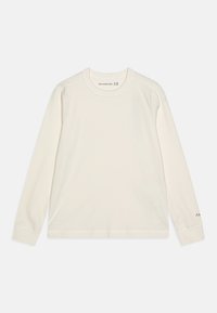 Cream long-sleeve shirt with a round neckline, ribbed texture, and a small logo in a contrasting color on the sleeve.
