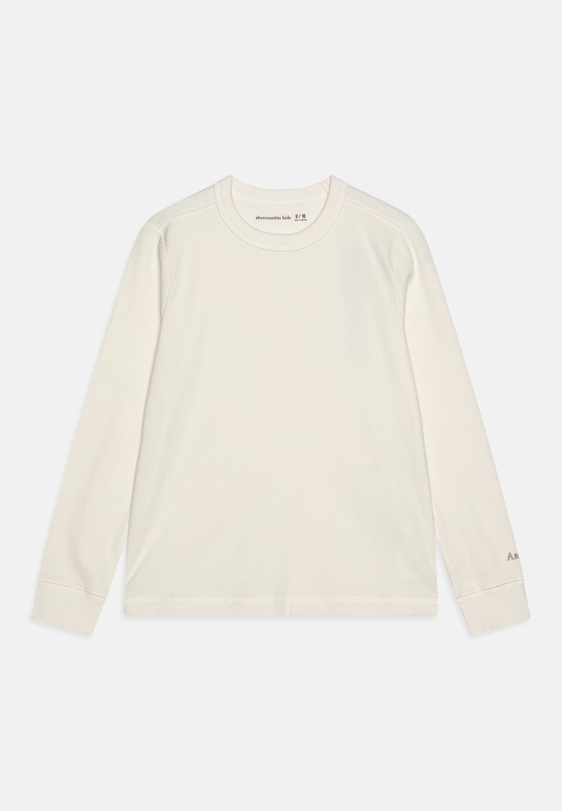 Cream long-sleeve shirt with a round neckline, ribbed texture, and a small logo in a contrasting color on the sleeve.