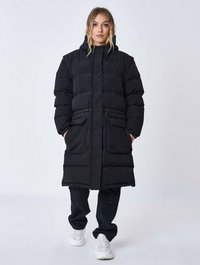 Sort puffjakke med hætte, der har lynlåslukning, to forlommer og quiltet tekstur. Båret med sorte bukser og hvide sneakers.