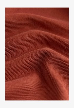 Rust-colored fabric with a soft, textured surface, featuring a fine knit pattern and gentle waves, highlighting its flexibility and drape.