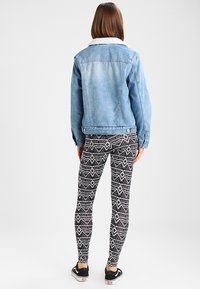 Giacca di jeans con un lavaggio chiaro e colletto in pelliccia sintetica, abbinata a leggings con fantasia bianca e nera a vita alta e sneakers nere.