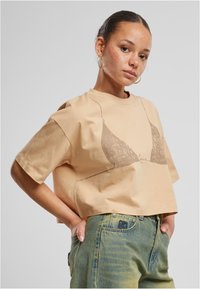 Kreemi värvi lühikeste varrukatega t-särk, mis on valmistatud pehmest puuvillast, millel on graafiline prinditud rinnahoidja kontuur tumedamas toonis. Omab ümmargust kaelust.