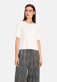 White short-sleeve t-shirt with a round neckline, made of soft fabric. Paired with pleated gray trousers featuring a vertical stripe pattern.