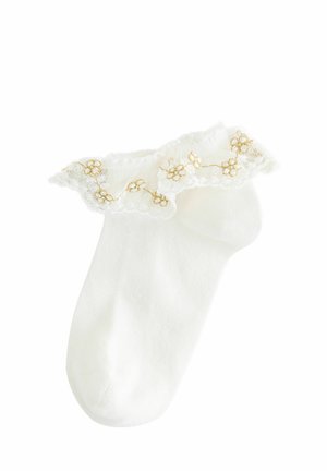 Biała skarpetka do kostki z falbaną z koronki na górze, z złotym haftem kwiatowym i miękką, gładką teksturą. Brak wzorów na ciele skarpetki.