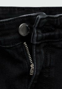 Gros plan sur un jean en denim noir ouvert avec un bouton métallique visible et des détails de la fermeture éclair.