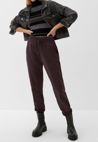 Giubbotto di jeans nero sopra un maglione a righe, abbinato a pantaloni della tuta viola e stivaletti neri chunky alla caviglia, con vita elasticizzata e tasche laterali.