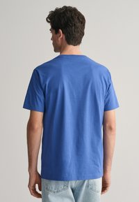 Tricou din bumbac albastru, cu mânecă scurtă și decolteu rotund, are o tivă dreaptă și o croială lejeră, evidențiind o textură netedă și un design minimalist.