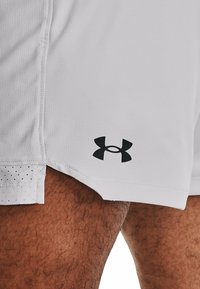 Pantalones cortos de rendimiento blancos con un acabado texturizado, que presentan un logo negro de Under Armour en el dobladillo y un acento perforado en el borde.