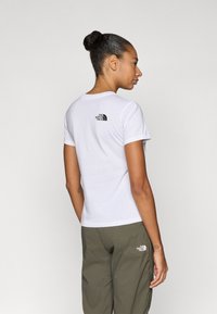 Άσπρο βαμβακερό T-shirt με στρογγυλή λαιμόκοψη, με μικρό μαύρο λογότυπο στην πλάτη. Συνδυάζεται με παντελόνι χρώματος ελιάς.