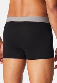 Bóxer de algodón negro con una cinturilla elástica gris, forma ajustada y un corte de pierna corto, que presenta una textura suave y costuras mínimas.