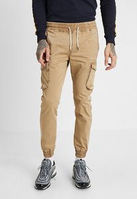 Beige cargobroek met een slim fit, elastische tailleband, trekkoordsluiting en zijzakken. Het materiaal is lichtgewicht met een gladde textuur.