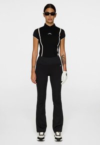 Svart atletisk pikétröja med vita detaljer, figursydd design. Svarta utsvängda byxor och vit handske. Svartvita sneakers fulländar looken.