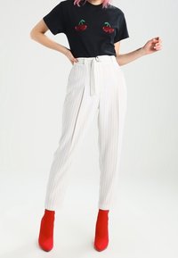 Svart t-shirt med körsbärsdetaljer, vita randiga byxor och röda klackade ankelskoot, som visar en figurnära design och hög midja.