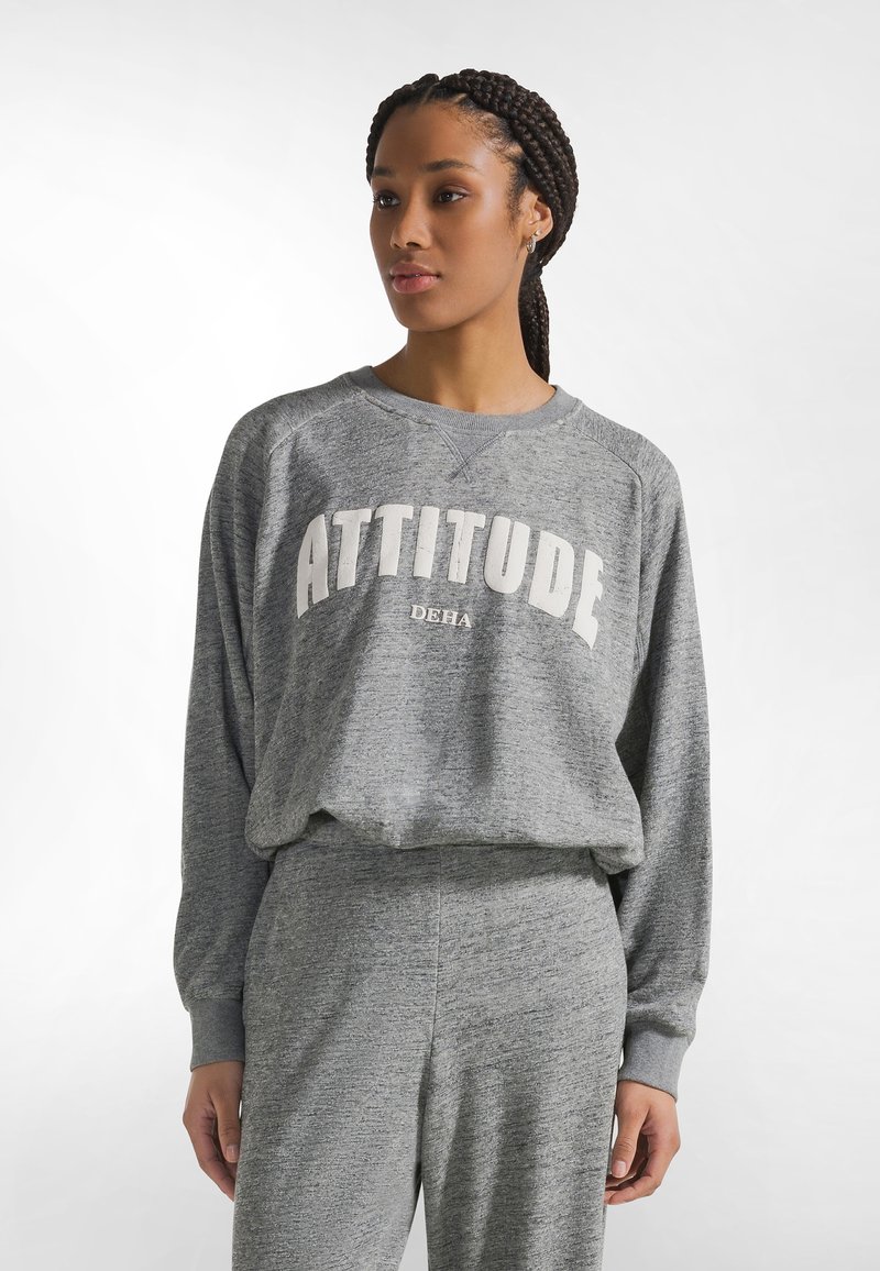 Sudadera gris con "ACTITUD" en blanco, con un ajuste relajado y cuello redondo. Tejido suave, puños acanalados y diseño ligeramente cropped.