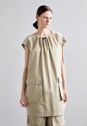 Beige, loose-fitting garment with short sleeves, gathered neckline, and drawstring. Features two large front pockets and a soft texture.