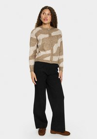 Brūns un bēšs svītrots kardigans ar apaļu apkakli un pogām, kombinēts ar melniem plašiem biksēm un brūnām kurpēm. Vienkāršs dizains un tekstūras.