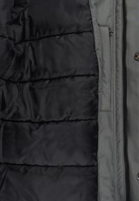 Gros plan de l’intérieur d’une veste matelassée noire et du panneau à fermeture éclair gris avec boutons-pression, montrant la texture du tissu et les détails des coutures.