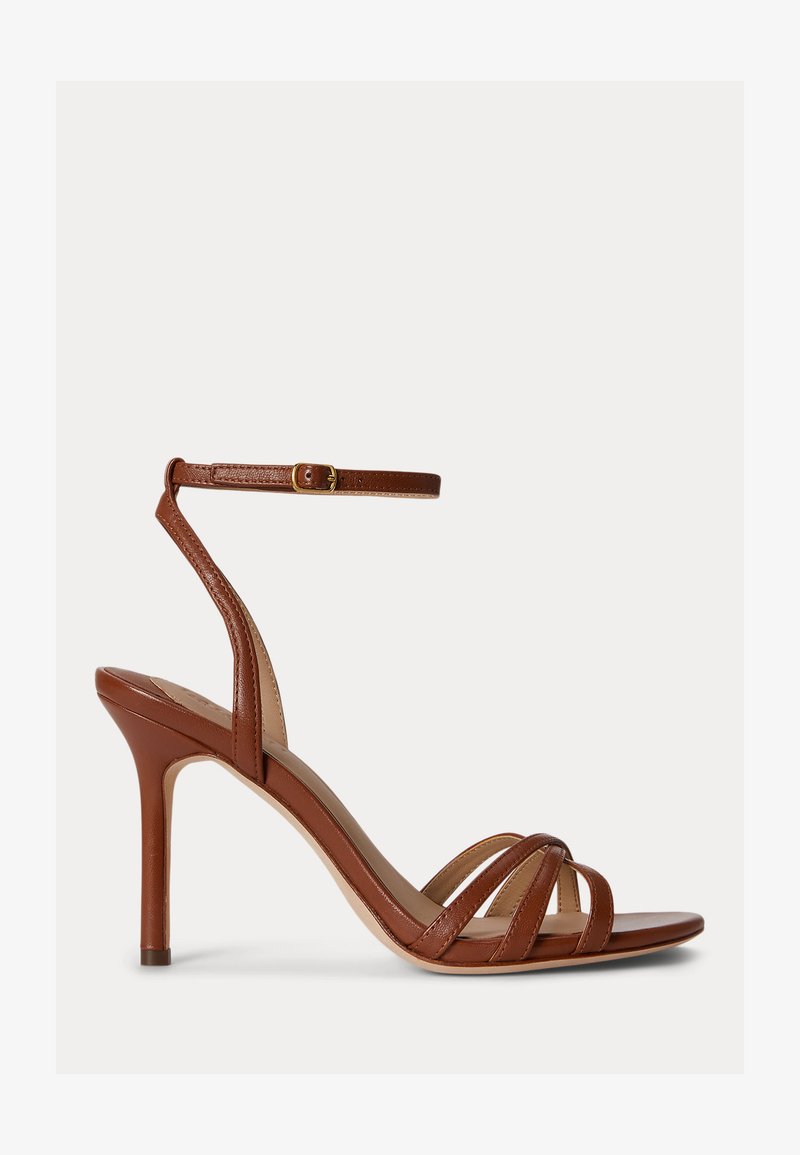 Καφέ δερμάτινο σανδάλι με ψηλό τακούνι, λεπτά λουράκια πάνω στα δάχτυλα και λουράκι αστραγάλου με χρυσή αγκράφα, εμφανιζόμενο σε πλευρική όψη σε λευκό φόντο.