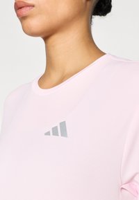 Αθλητική μπλούζα σε ανοιχτό ροζ χρώμα με στρογγυλή λαιμόκοψη και γκρι λεπτομέρεια λογότυπου στο αριστερό μέρος του στήθους, από υφή υφάσματος με ανάγλυφη επιφάνεια.